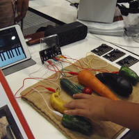 写真は、野菜や果物を使ってiPad用の楽器アプリを操作しているところ
