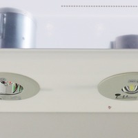 ハロゲン電球非常用照明器具「IEM-13221HN」（左）とLED非常用照明器具「LEDEM13221」（右）。「IEM-13221HN」に付いているヒモは、定期点検時に重りを吊るし、きちんと点灯するかを確認するためのもので、「LEDEM13221」はボタンのワンタッチ操作で点検が可能（撮影：防犯システム取材班）