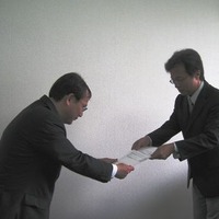 加藤博 総務省 九州総合通信局無線通信部長（右）から免許状を受領する西川嘉之 UQコミュニケーションズ 渉外部長（左）