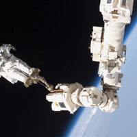 国際宇宙ステーションのロボットアームに足を固定して、ニコンの機材で撮影するロビンソン宇宙飛行士