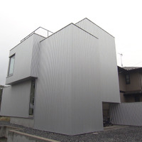 シルバーのガルバリウム鋼板に覆われ、窓が１つもない正面側の外観©MBS