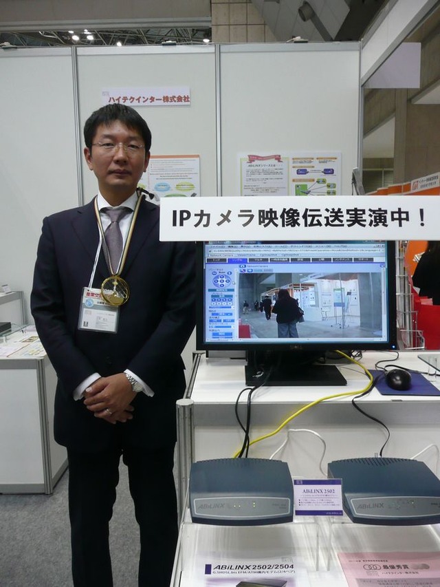 同社のブース内にて、代表取締役 亘尾紀人氏。ABiLINXシリーズを用いて、IPカメラによる画像伝送のデモも実施