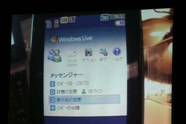 FOMAでもメッセンジャーが使える。携帯電話に小型カメラを固定して、通信の様子をプロジェクタに映したデモ