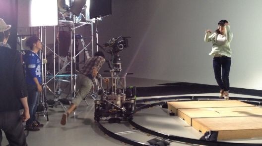 スタジオ（仙台市内）でのTVCM撮影風景：中央でジャンプする出演者と人力でカメラを動かすスタッフ。