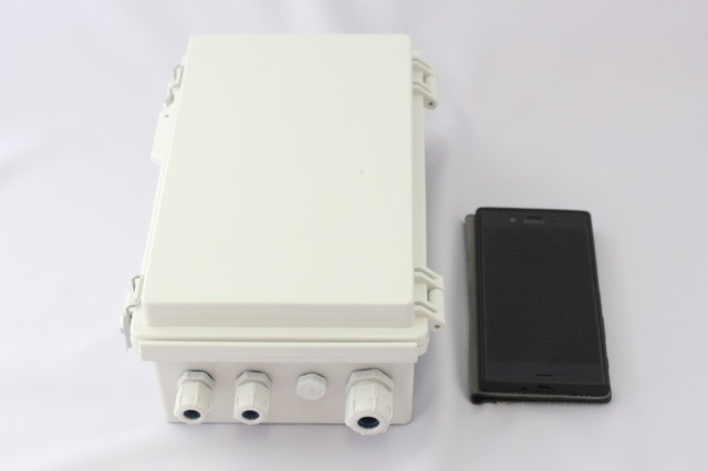 フタを閉じた状態の「Coral Edge BOX」とスマートフォン（Xperia XZ）とのサイズ比較。ケース自体は、IP65相当の防塵防水対応で、内部の構成機器に関しても、動作温度が-30～70度と屋外設置を想定した仕様になっている（撮影：防犯システム取材班）