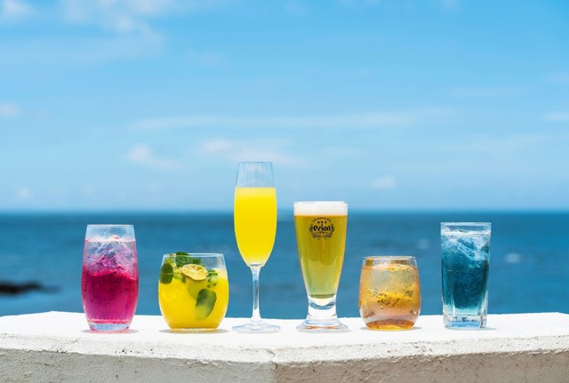 ドリンク左から【カフェンチュ】「WATTA パッションフルーツ カフェンチュオリジナルアレンジ『北谷サンセット』」801円（1杯）【オッチサイダリー】「occi シークヮーサーノンアルモヒート」 イートイン 880円（1杯）、「occi シークヮーサースパークリングワイン」 イートイン 990円（1杯）【オリオンビール】「オリオン生ビール」 601円（1杯）【カフェンチュ】「ルートビアシュナップス」 801円（1杯）、「WATTA 雪塩シークヮーサー カフェンチュオリジナルアレンジ『青の洞窟』」801円（1杯）